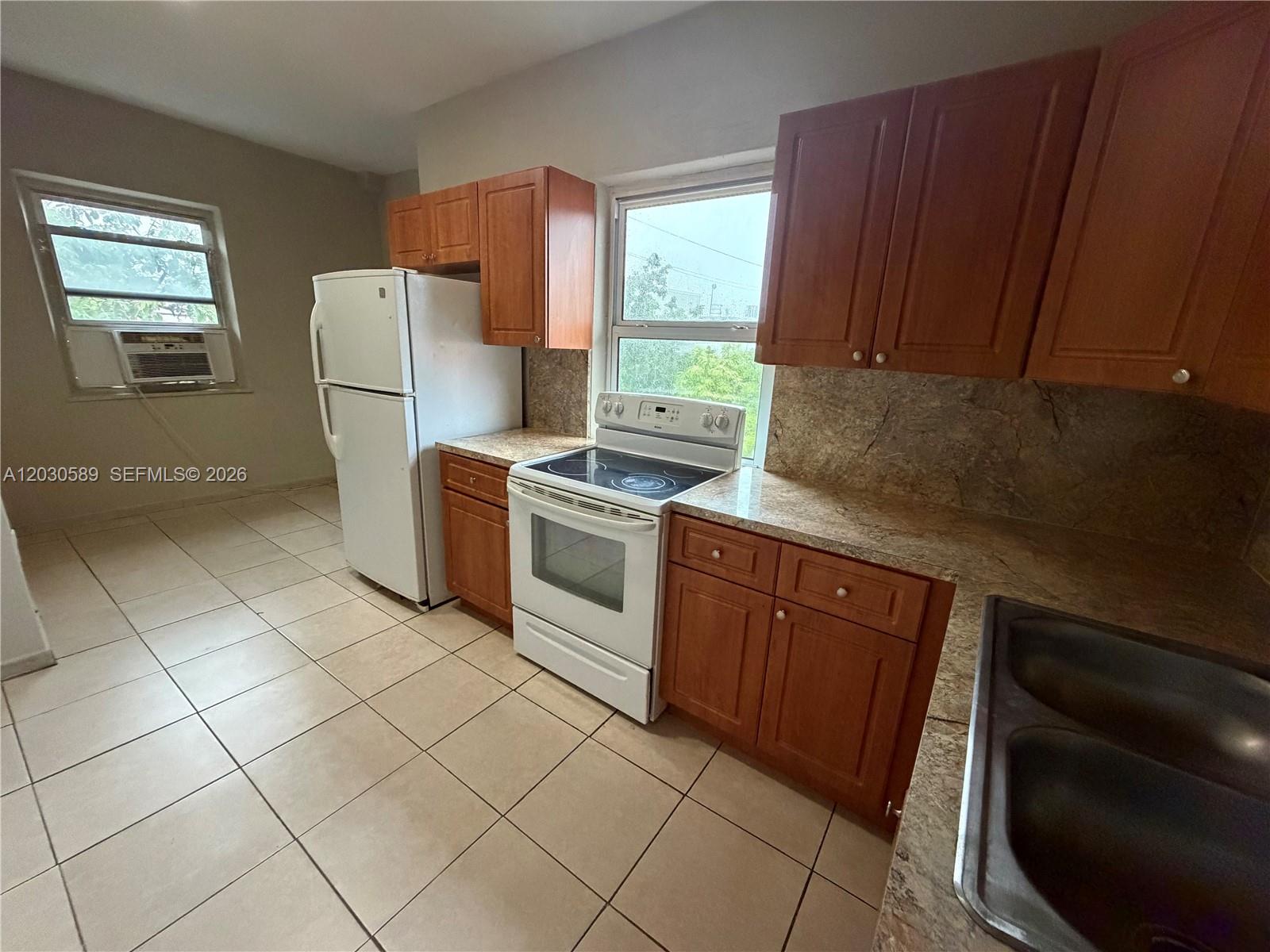 A kitchen features wood cabinets, granite countertops, white appliances, and light-colored floor tiles — 1422 NW 26th Ave, Miami FL 33125, MIAMI, FL