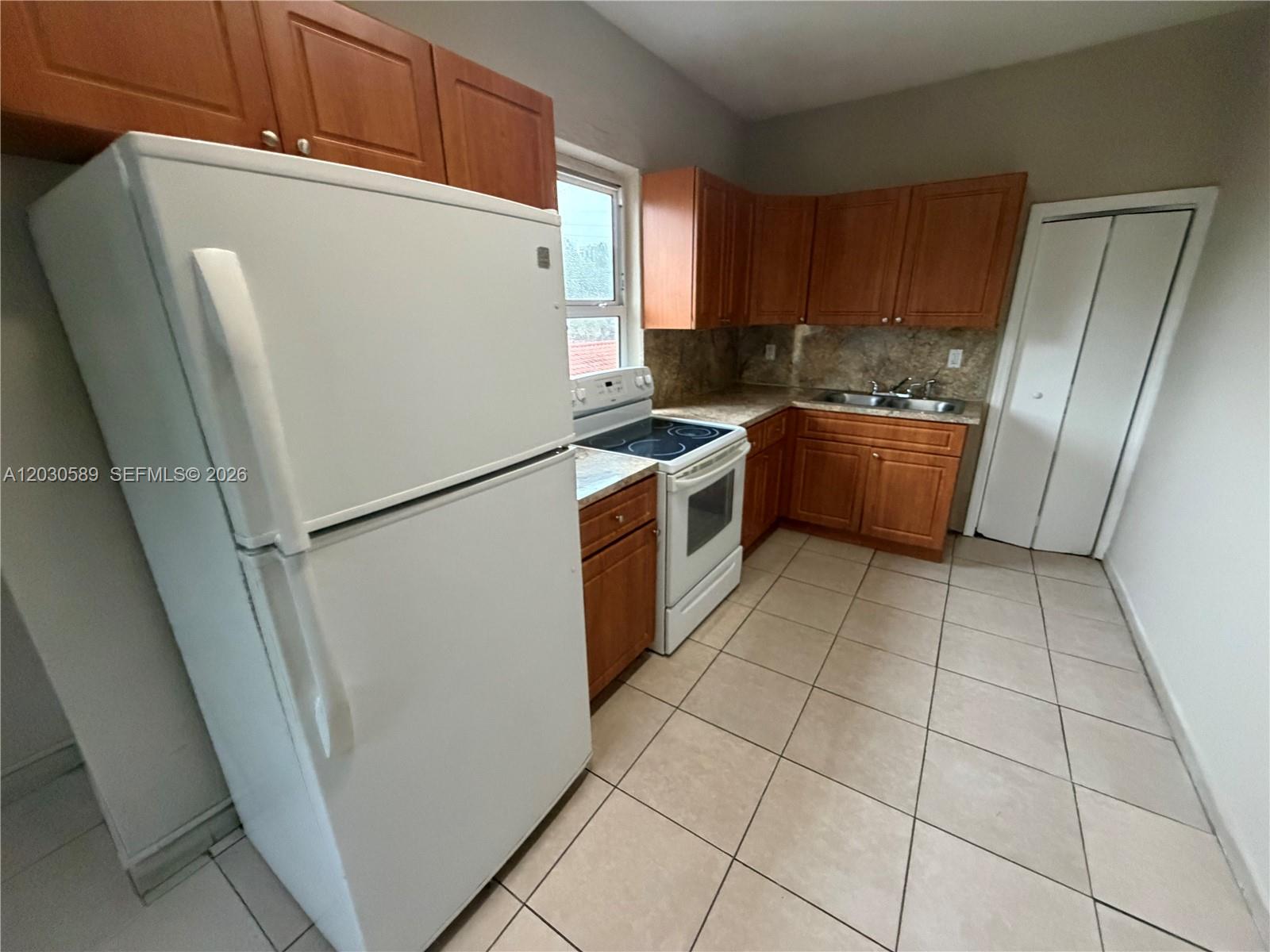 A kitchen features wood cabinets, a white refrigerator, a stove, and light-colored tile flooring — 1422 NW 26th Ave, Miami FL 33125, MIAMI, FL