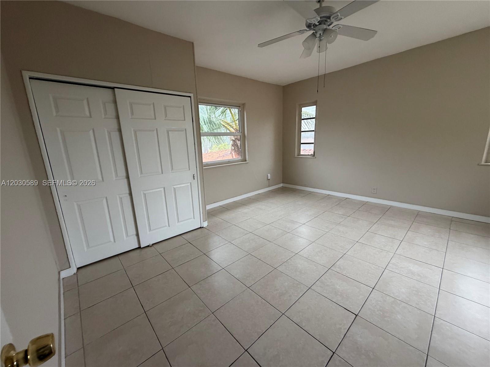 An empty bedroom features beige walls, tiled flooring, a ceiling fan, and sliding closet doors — 1422 NW 26th Ave, Miami FL 33125, MIAMI, FL