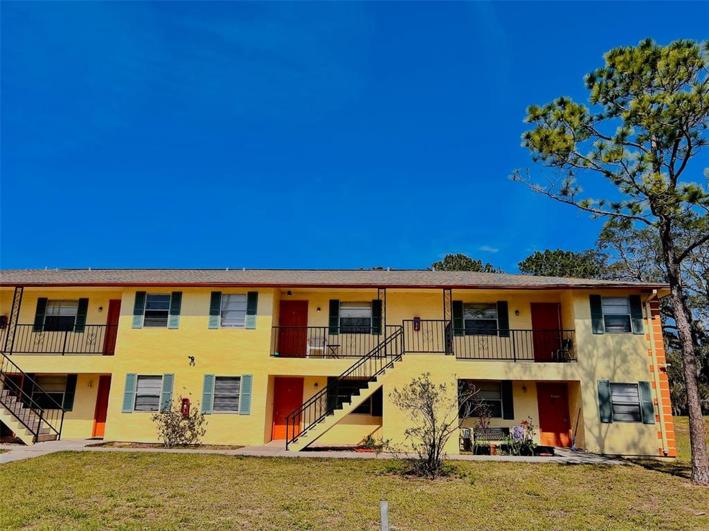 A two-story yellow apartment building features black railings, green shutters, and an exterior staircase — 2192 KNOX MCRAE DRIVE UNIT 1, TITUSVILLE, FL
