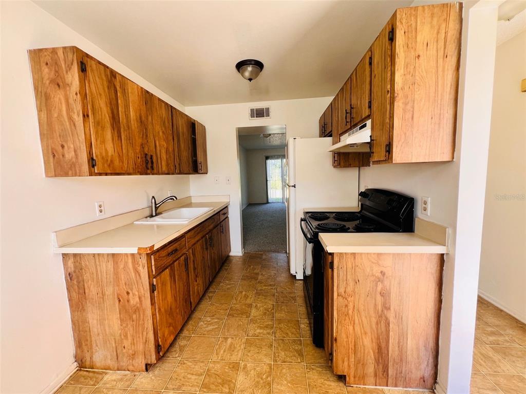 A kitchen features wood cabinets, laminate countertops, a black stove, and tan tile flooring — 2192 KNOX MCRAE DRIVE UNIT 1, TITUSVILLE, FL
