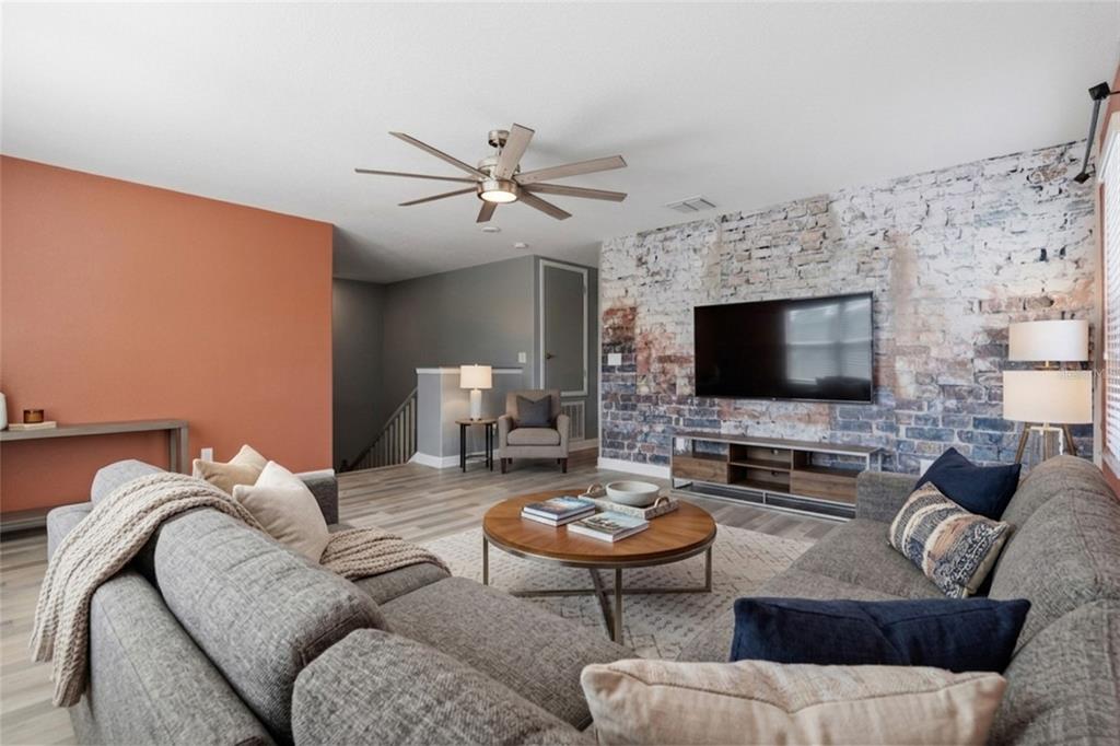 A living room features a brick accent wall, a gray sectional, and a ceiling fan — 13917 ROSEATE TERN LANE, RIVERVIEW, FL