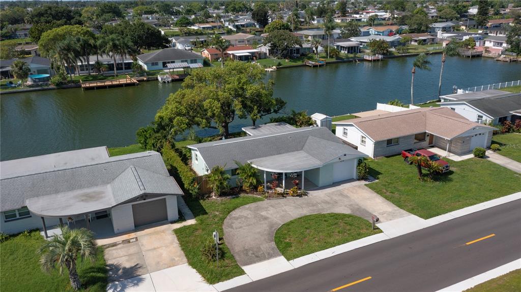 An aerial view shows three suburban houses with driveways and lawns bordering a canal — 4114 SUNRAY DRIVE, HOLIDAY, FL