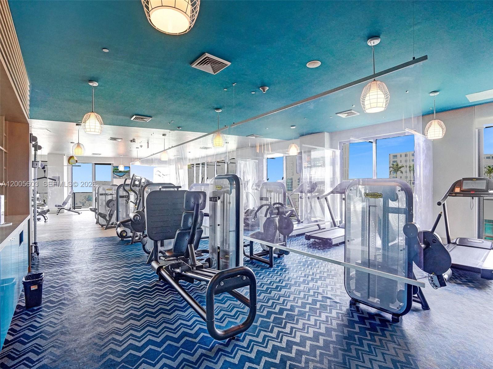 A gym features exercise equipment, a blue chevron-patterned floor, and a teal ceiling with pendant lights — 121 NE 34th St # 1806A, Miami FL 33137, MIAMI, FL
