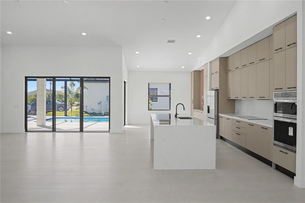 A modern kitchen features light-toned cabinetry, a white quartz island, and sliding glass patio doors — 14687 LILLIAN CIRCLE, PORT CHARLOTTE, FL