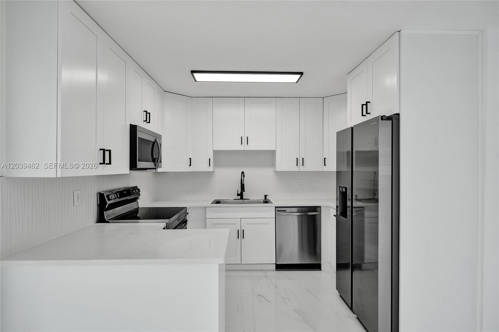 A modern kitchen features white cabinets, stainless steel appliances, and white marble-look flooring — 1220 NE 8 St, Pompano Beach FL 33060, POMPANO BEACH, FL