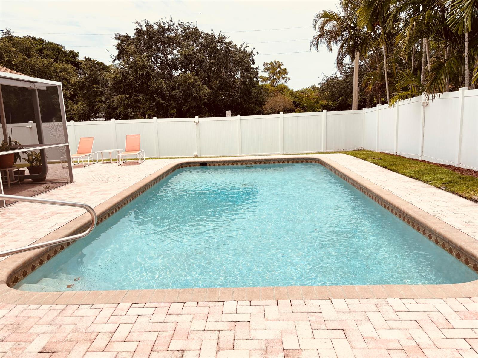 A rectangular swimming pool with a brick paver deck and a white vinyl privacy fence — 1076 SW 26th Terrace, Deerfield Beach FL 33442, DEERFIELD BEACH, FL