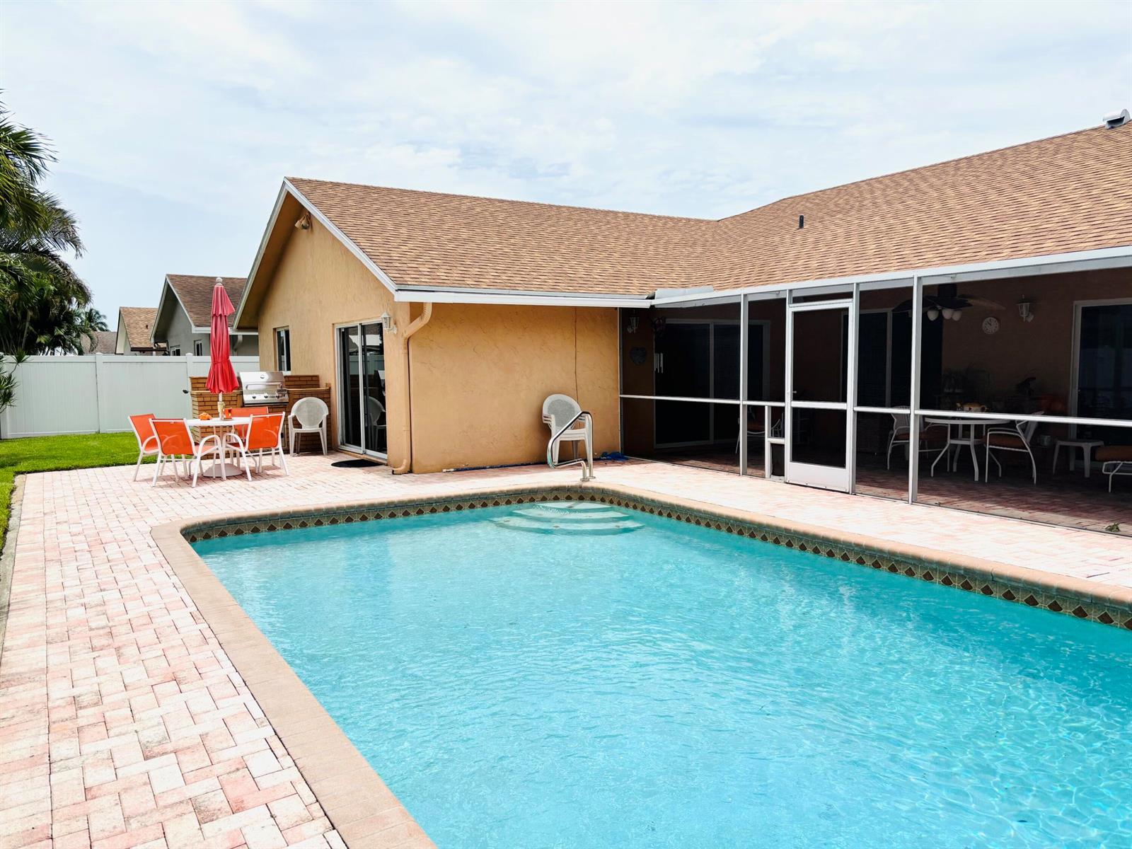 A swimming pool sits on a paved patio beside a house with a screened-in porch — 1076 SW 26th Terrace, Deerfield Beach FL 33442, DEERFIELD BEACH, FL