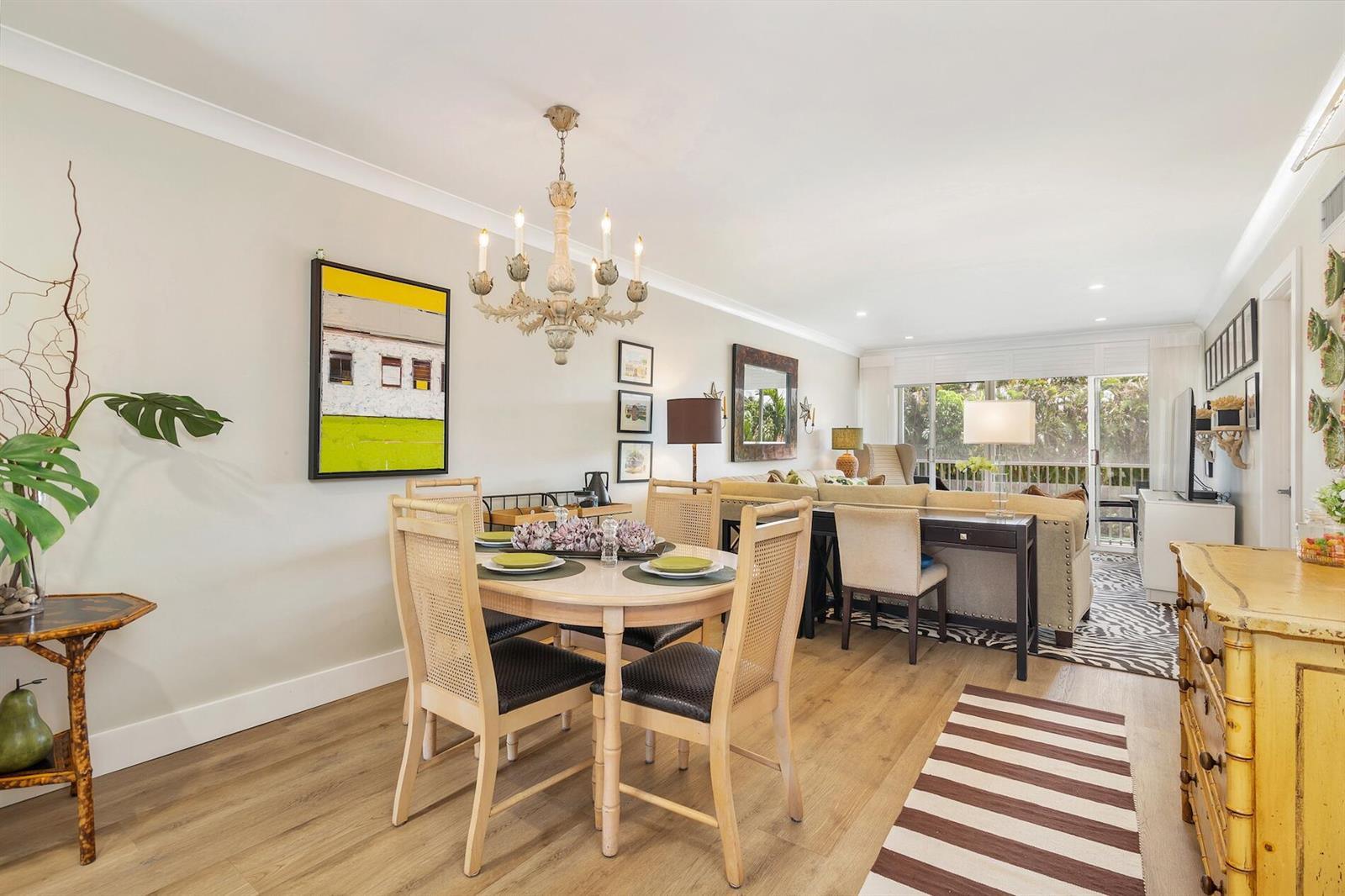 A dining area with a round table and chandelier opens into a living room space — 1910 S Ocean Boulevard # 224, Delray Beach FL 33483, DELRAY BEACH, FL