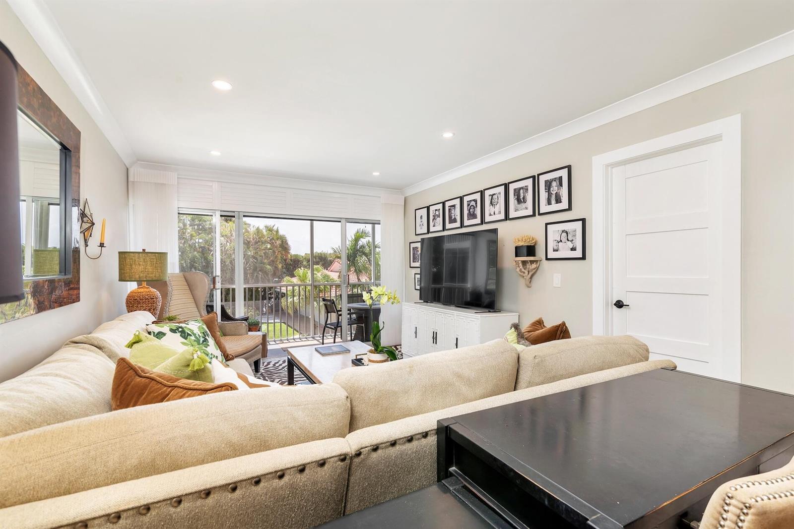 A living room features a beige sectional sofa, a television, and a balcony with greenery — 1910 S Ocean Boulevard # 224, Delray Beach FL 33483, DELRAY BEACH, FL