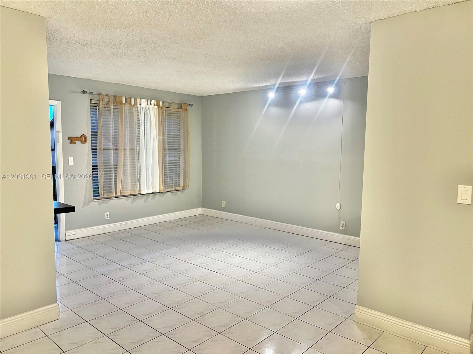 An empty room features light gray walls, white tile flooring, and a track lighting fixture — 10002 Winding Lake Rd # 203, Sunrise FL 33351, SUNRISE, FL