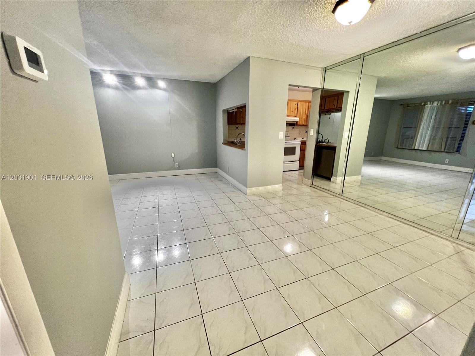 A room with white tile flooring, a pass-through window to the kitchen, and mirrored walls — 10002 Winding Lake Rd # 203, Sunrise FL 33351, SUNRISE, FL
