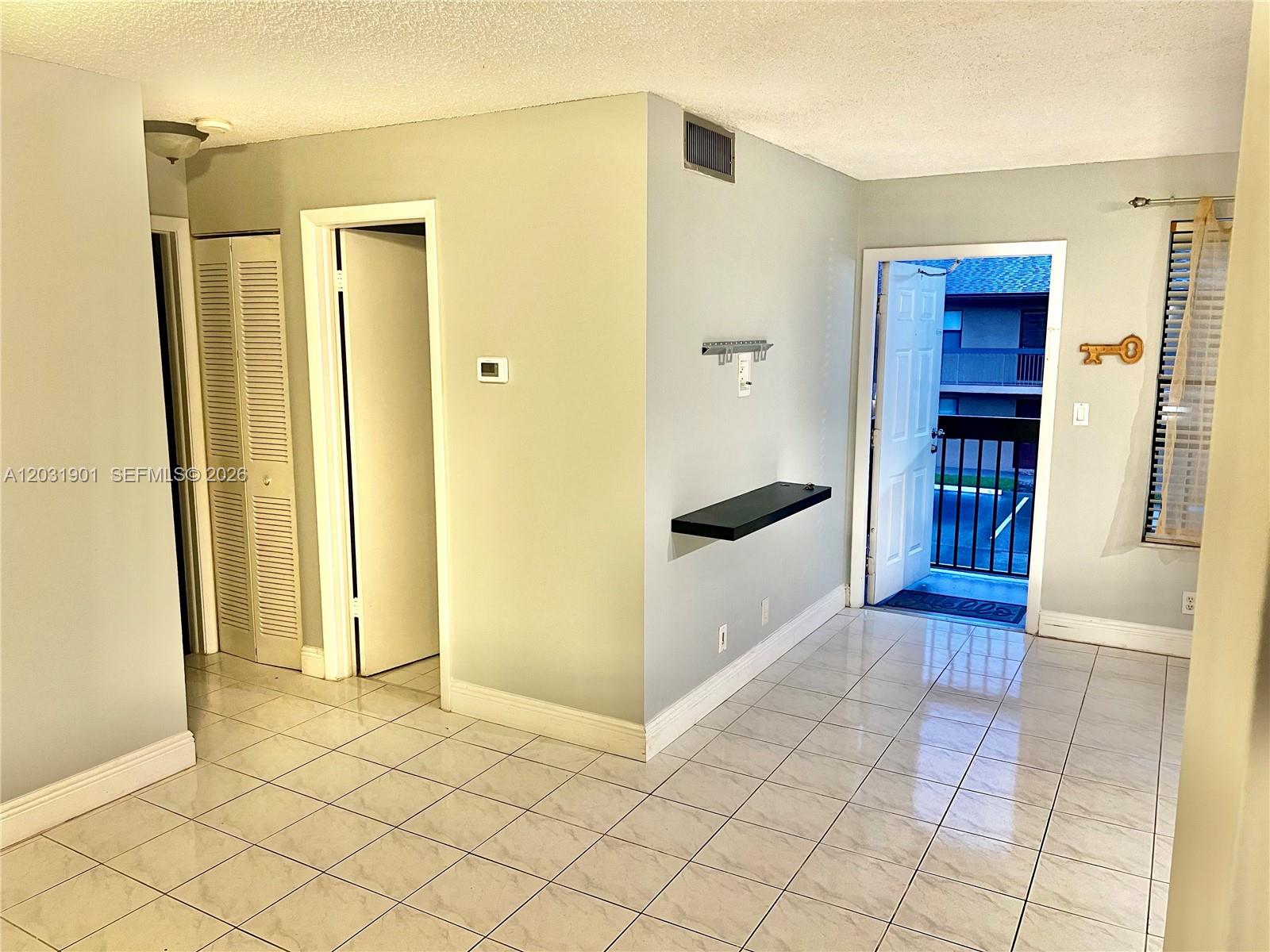 A tiled room features a floating shelf, a doorway to a balcony, and closet doors — 10002 Winding Lake Rd # 203, Sunrise FL 33351, SUNRISE, FL