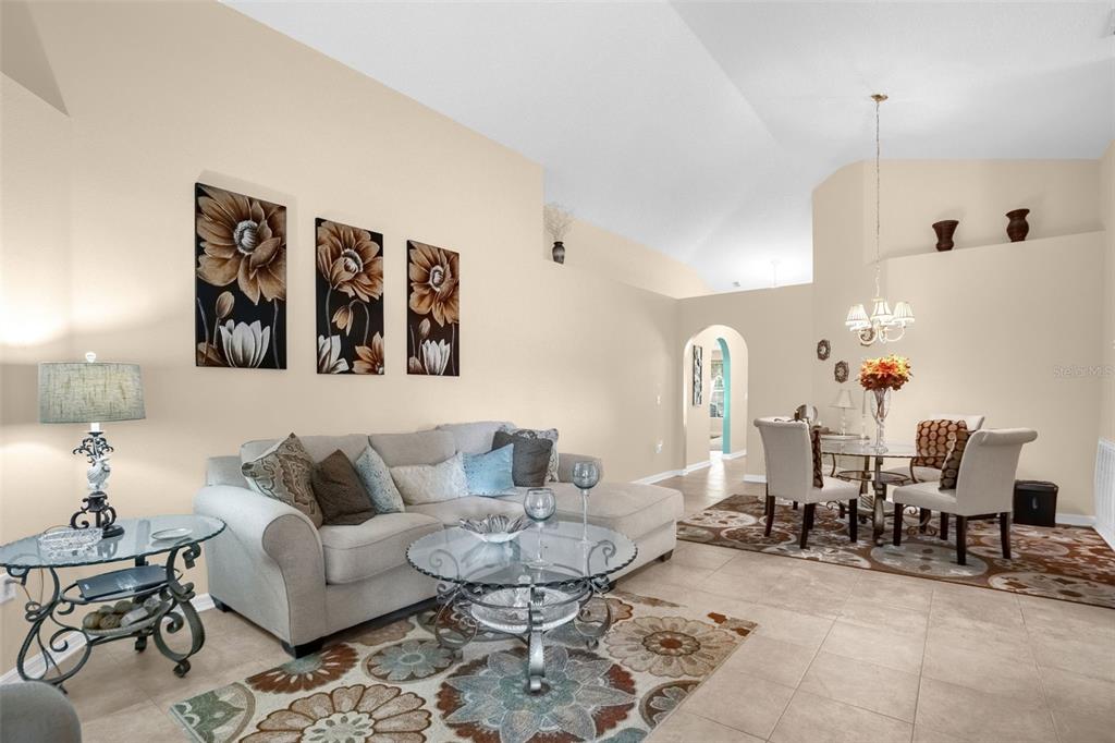 A living room and dining area with beige walls, tile floors, and a vaulted ceiling — 839 MARIETTA LANE, EUSTIS, FL