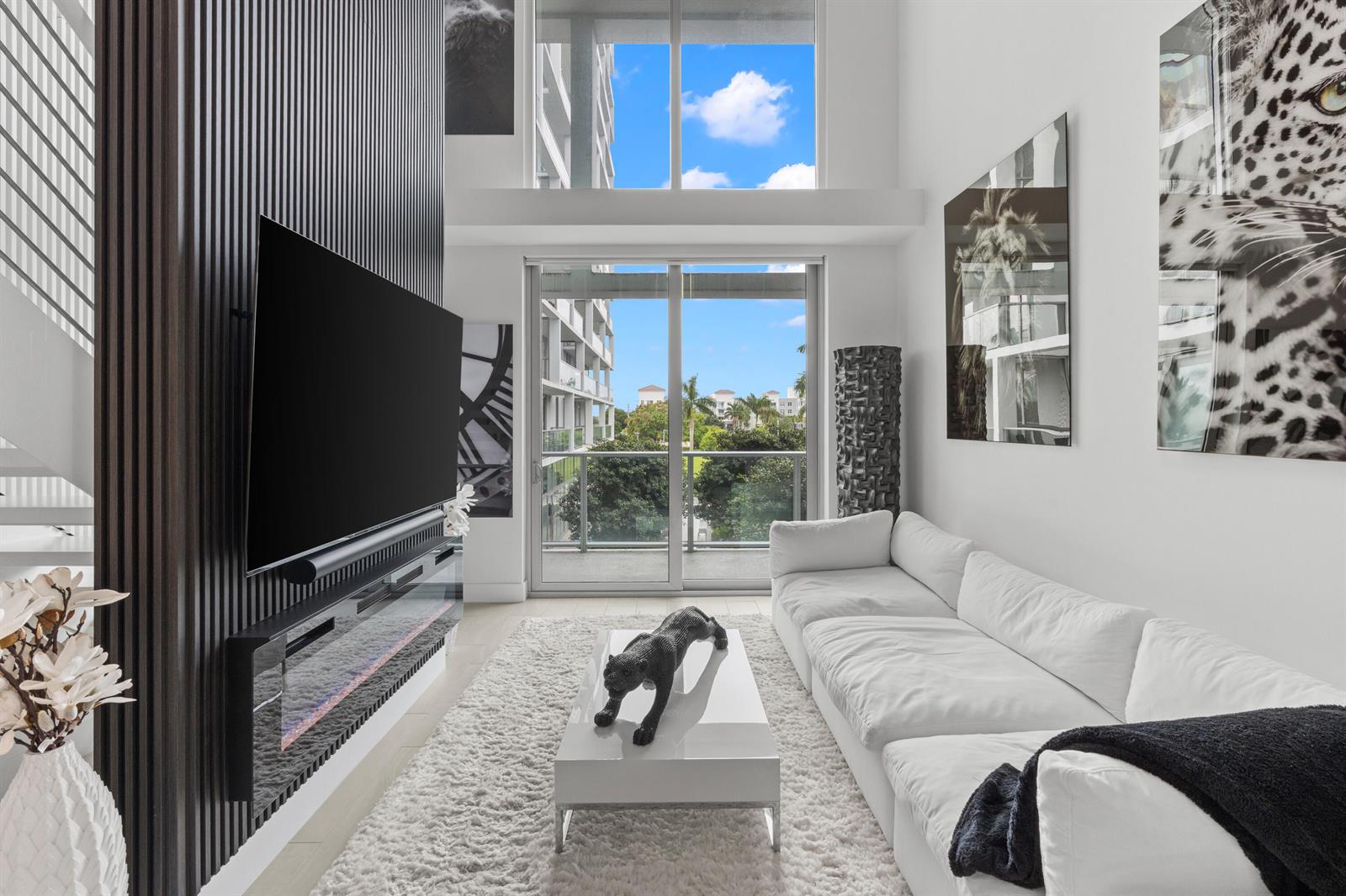 A modern living room features a white sectional, a fireplace, and floor-to-ceiling windows — 2000 Metropica Way # 214, Sunrise FL 33323, SUNRISE, FL