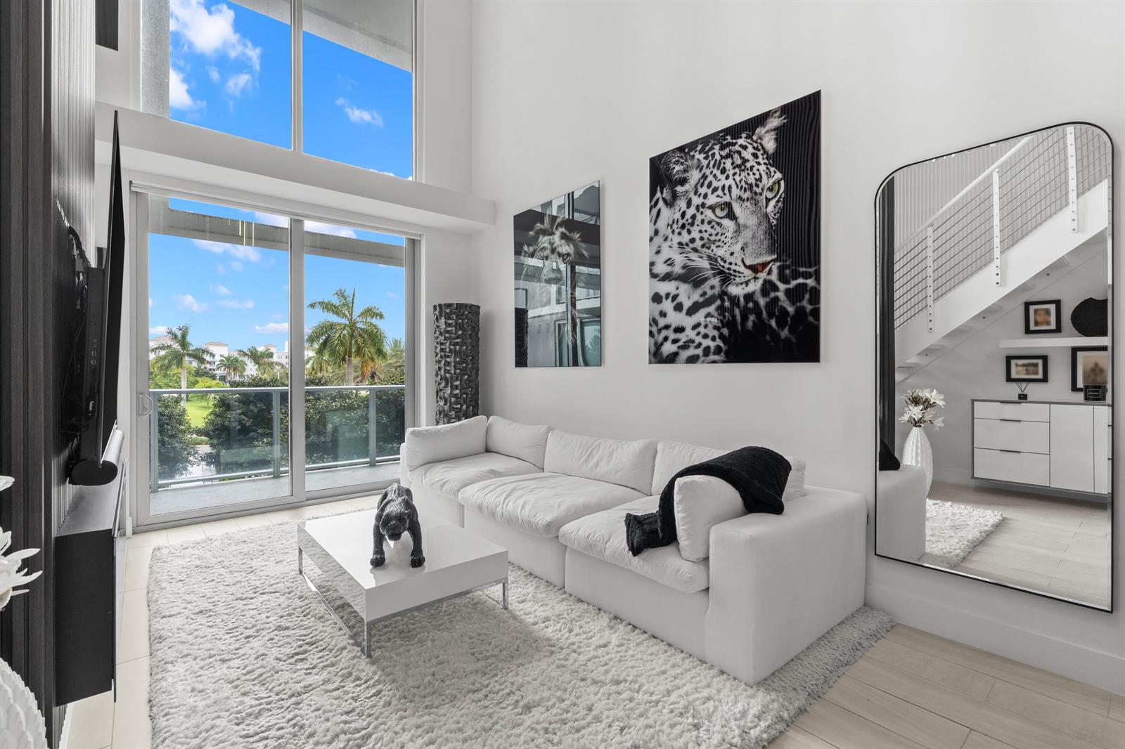 A modern living room features a white sectional sofa, a shag rug, and large wall art — 2000 Metropica Way # 214, Sunrise FL 33323, SUNRISE, FL