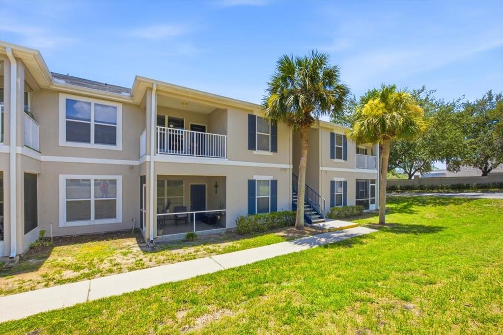 A two-story apartment building with tan stucco walls, blue shutters, and a ground-level screened patio — 4008 HEMINGWAY CIRCLE, HAINES CITY, FL