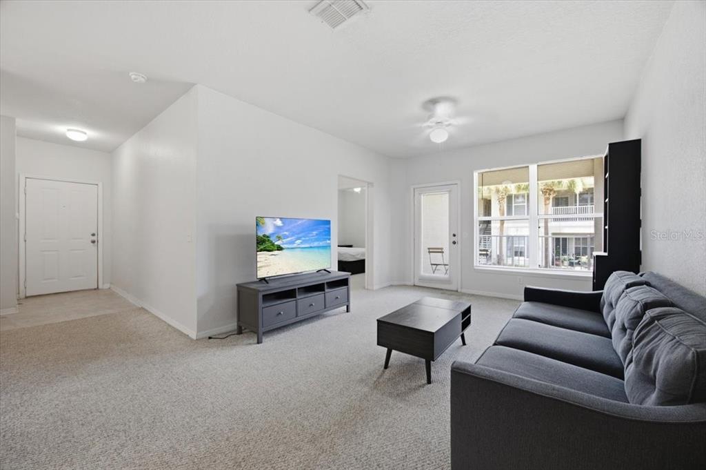 A living room with a gray sofa, coffee table, television on a stand, and balcony access — 4008 HEMINGWAY CIRCLE, HAINES CITY, FL
