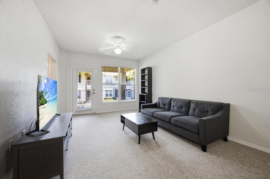 A living room features a gray sofa, coffee table, media console, and a glass door — 4008 HEMINGWAY CIRCLE, HAINES CITY, FL