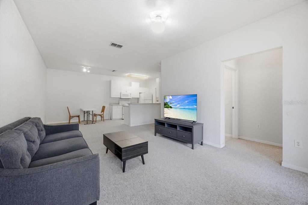 A living room with gray carpet, a dark sofa, a coffee table, and an open kitchen — 4008 HEMINGWAY CIRCLE, HAINES CITY, FL