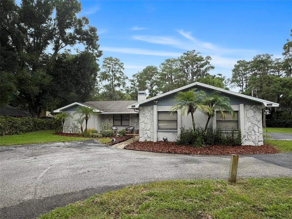 A single-story house with a stone facade, gray siding, and a large asphalt driveway — 18306 CRAWLEY ROAD, ODESSA, FL