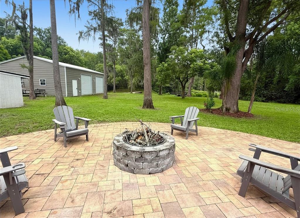 A stone fire pit sits on a paved patio surrounded by chairs in a grassy yard — 18306 CRAWLEY ROAD, ODESSA, FL