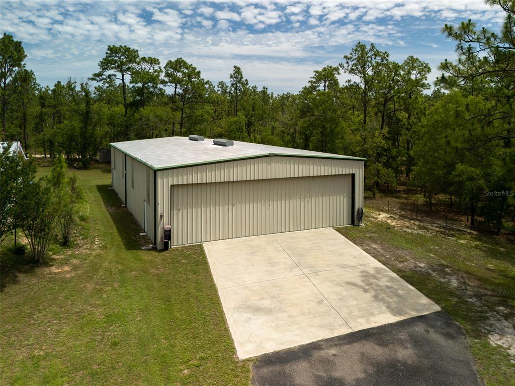 An aerial view of a metal workshop building with a concrete driveway and surrounding trees — 267 MELROSE LANDING DRIVE, HAWTHORNE, FL