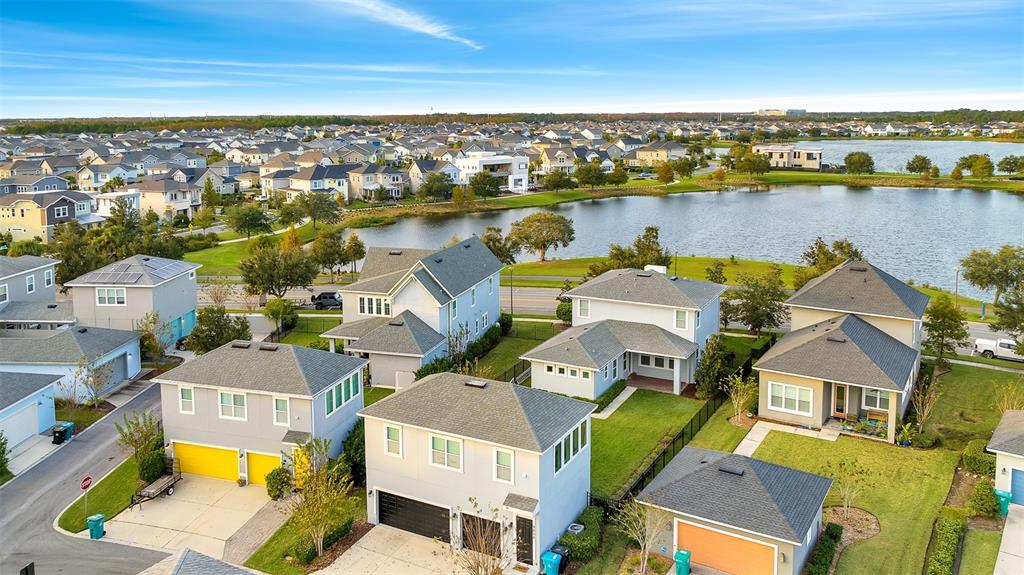 An aerial view shows several suburban houses with garages and driveways near a large lake — 9044 TAVISTOCK LAKES BOULEVARD, ORLANDO, FL