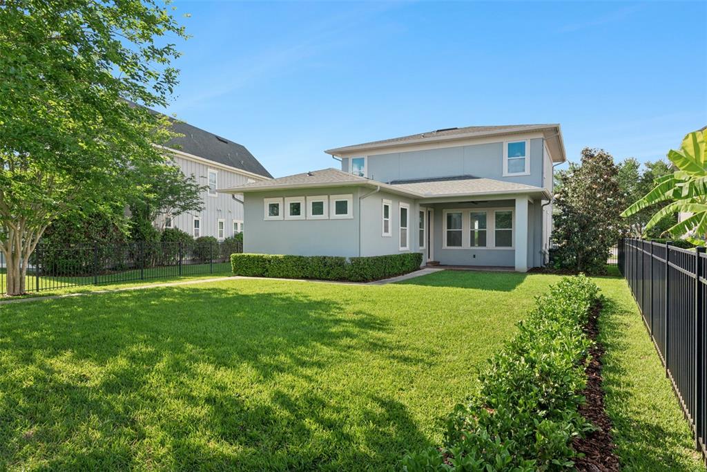 The backyard features a green lawn, a hedge, a black fence, and a two-story house — 9044 TAVISTOCK LAKES BOULEVARD, ORLANDO, FL