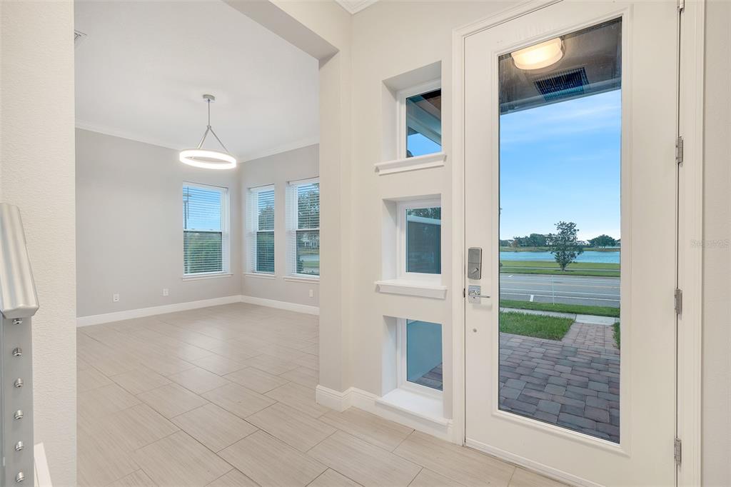 A bright entryway with tile flooring, three small square windows, and a view of a lake — 9044 TAVISTOCK LAKES BOULEVARD, ORLANDO, FL