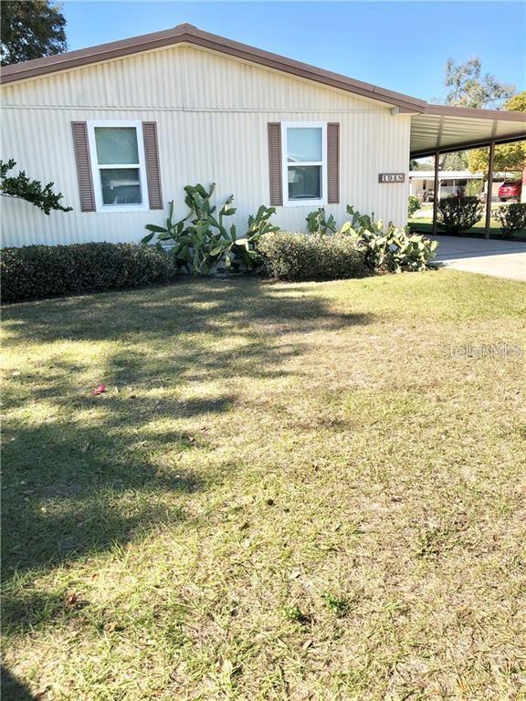 A single-story house with light-colored siding, a carport, and landscaping in the front yard — 1948 REGINA DRIVE, LAKE ALFRED, FL