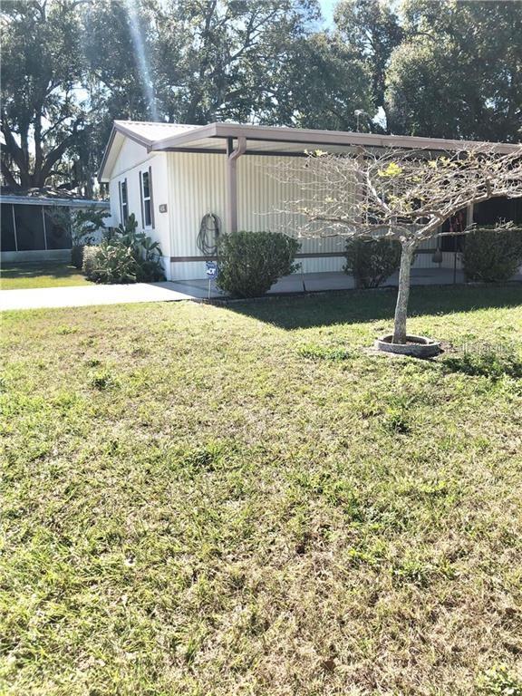 A single-story mobile home with a carport and a small tree in the front yard — 1948 REGINA DRIVE, LAKE ALFRED, FL