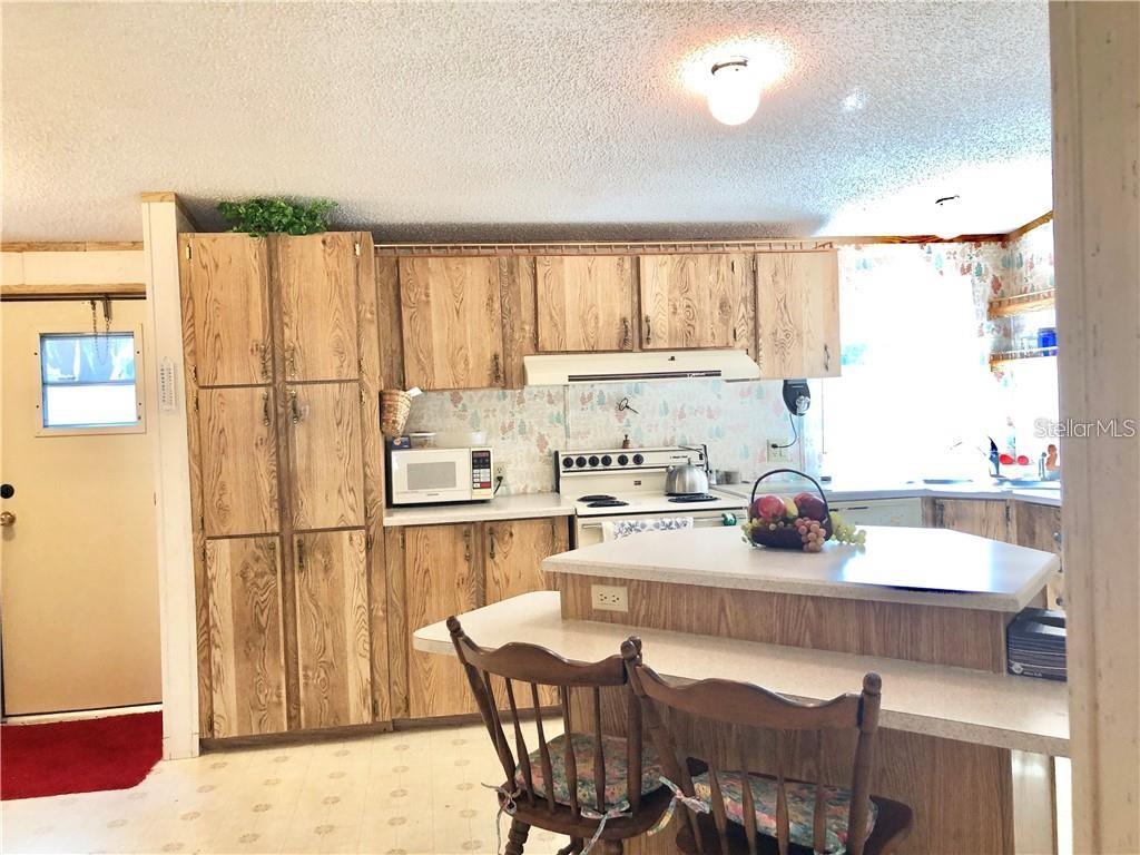 A kitchen features wood-grain cabinets, a white stove, a kitchen island, and a breakfast bar — 1948 REGINA DRIVE, LAKE ALFRED, FL