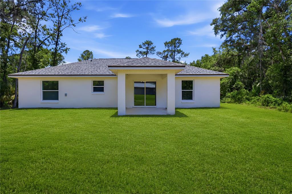 The rear exterior of a single-story house features a covered patio and a grassy yard — 3 SEQUOIA DRIVE TRACE, OCKLAWAHA, FL