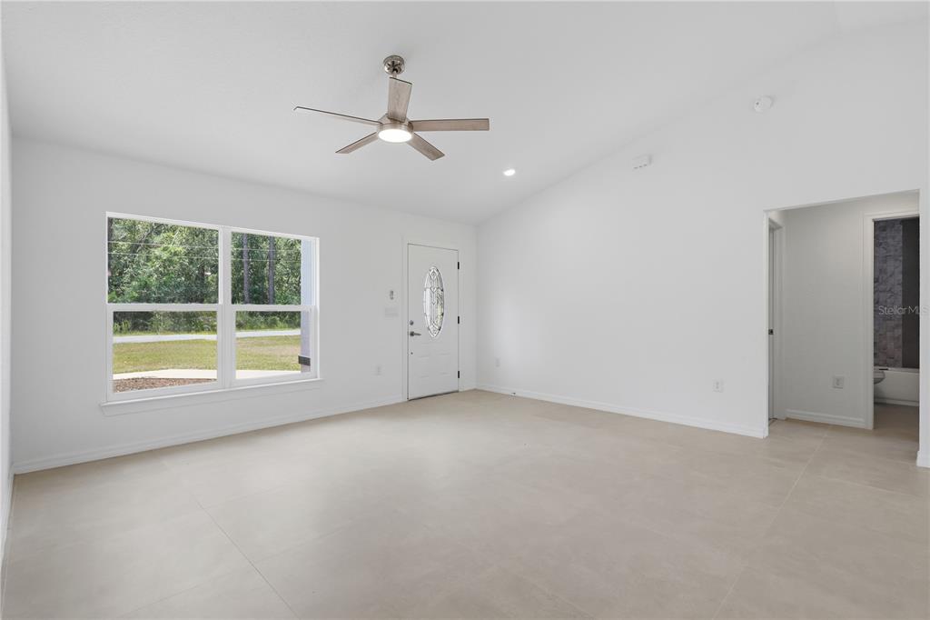 A bright, empty living room features white walls, tile flooring, a ceiling fan, and an entryway — 3 SEQUOIA DRIVE TRACE, OCKLAWAHA, FL