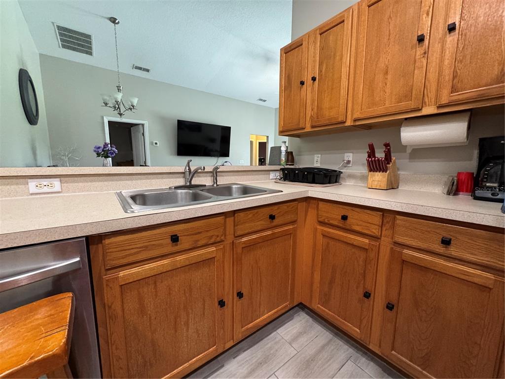 A kitchen features wood cabinets, a double-basin sink, and a countertop overlooking a living area — 1126 SANDY RIDGE DRIVE, DAVENPORT, FL