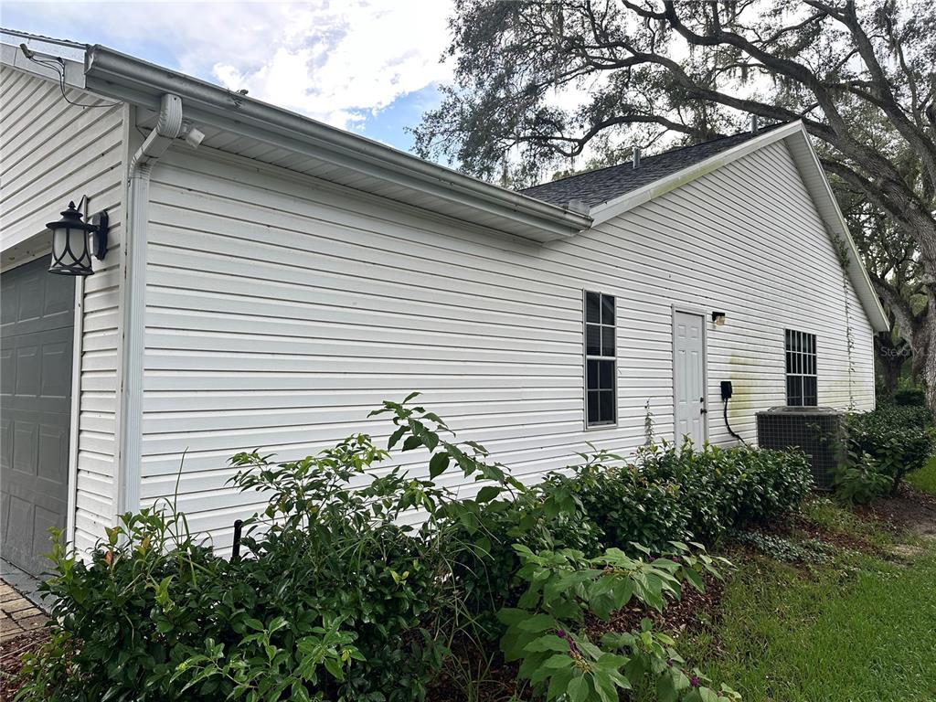 A side view of a white vinyl-sided house with a garage, windows, and landscaping — 4242 LEAFWAY CIRCLE, LEESBURG, FL