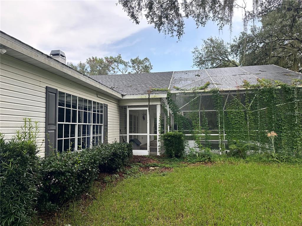A view of a house exterior with a screened-in pool enclosure and overgrown vegetation — 4242 LEAFWAY CIRCLE, LEESBURG, FL