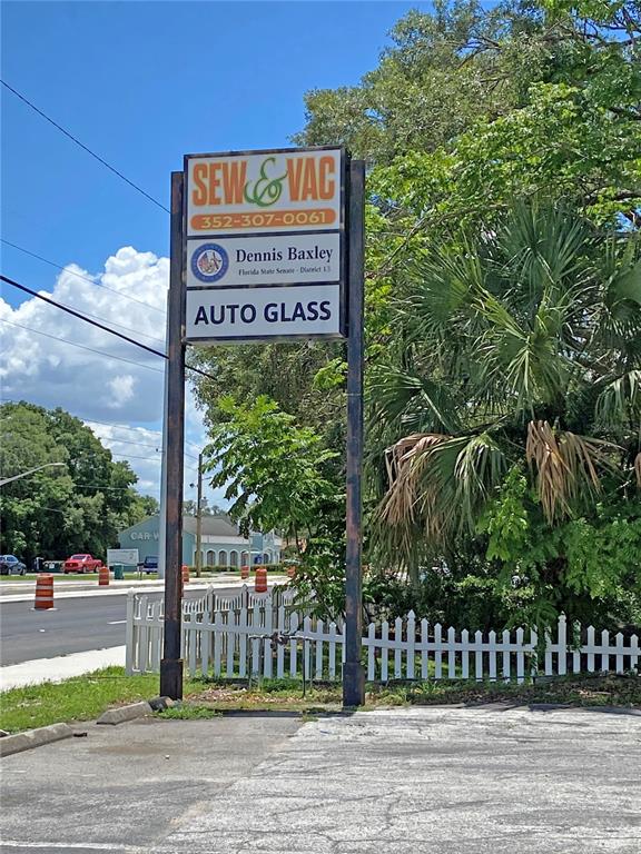 A tall, multi-tenant business sign stands near a white picket fence and a paved road — 206 S US HIGHWAY 27/441, LADY LAKE, FL