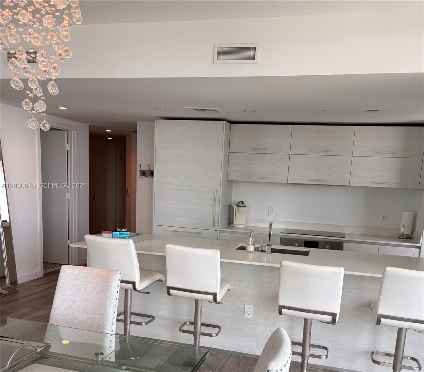 A modern kitchen features light wood cabinetry, a white island with bar stools, and a chandelier — 1300 S Miami Ave # 2205, Miami FL 33130, MIAMI, FL