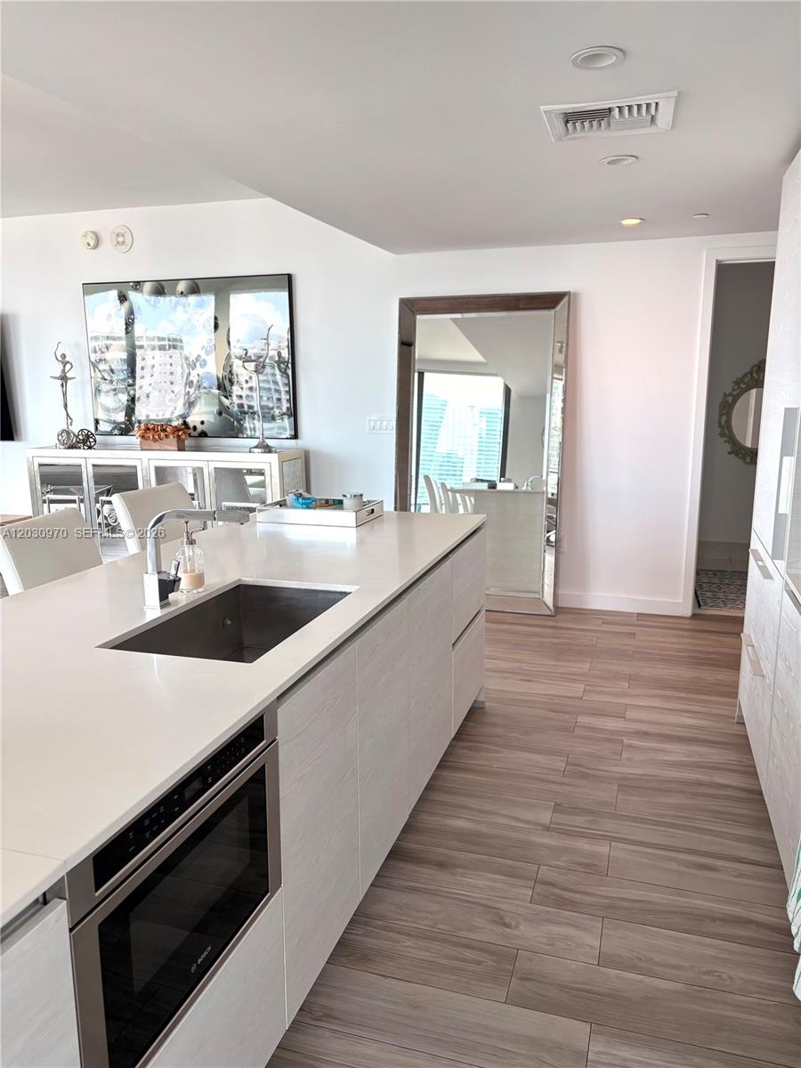 A modern kitchen features a white island with a built-in oven and wood-grain cabinetry — 1300 S Miami Ave # 2205, Miami FL 33130, MIAMI, FL