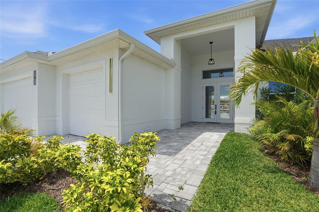 A white house exterior features a paved walkway leading to a double-door entryway and garage — 1625 SW 44TH TERRACE, CAPE CORAL, FL