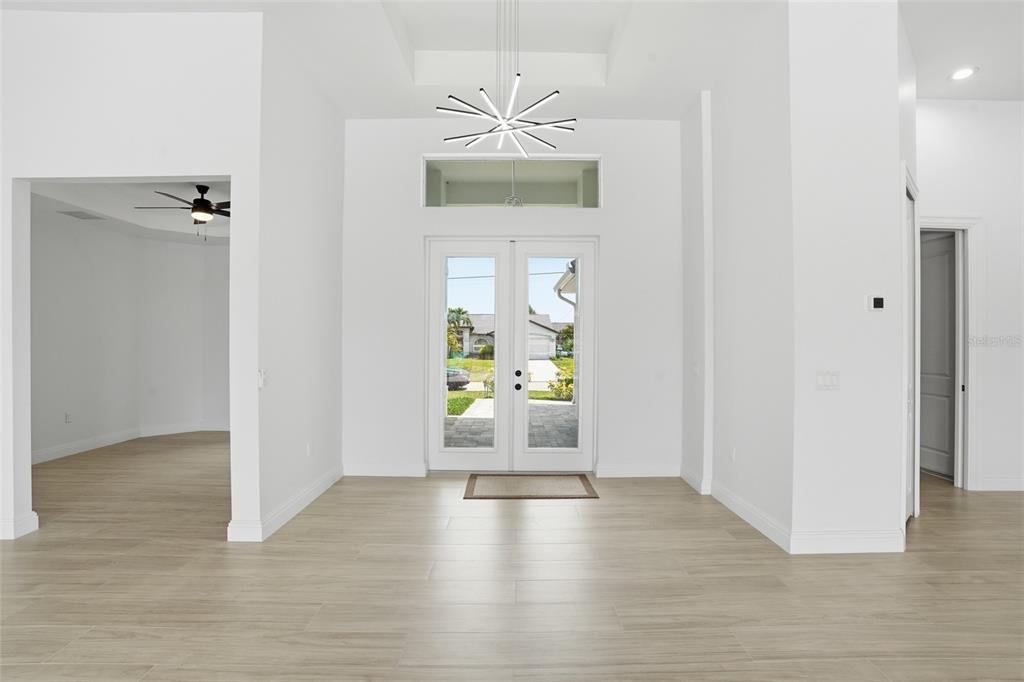 A bright entryway features light wood-look tile flooring, a modern chandelier, and double glass doors — 1625 SW 44TH TERRACE, CAPE CORAL, FL