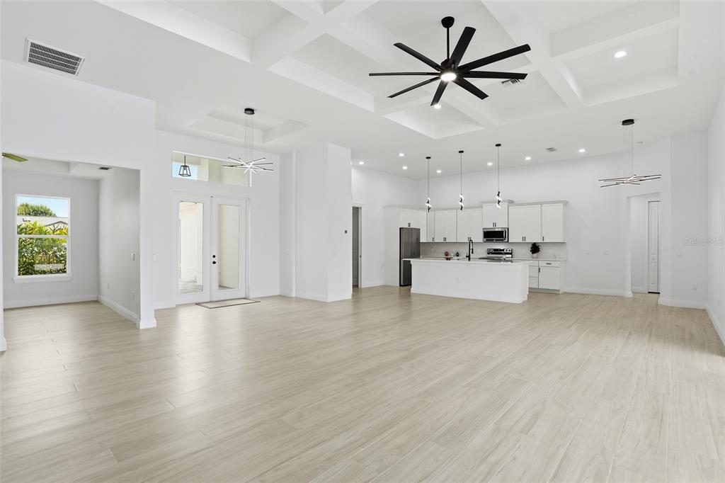 A bright, open-concept living area features a white kitchen, coffered ceilings, and light wood flooring — 1625 SW 44TH TERRACE, CAPE CORAL, FL