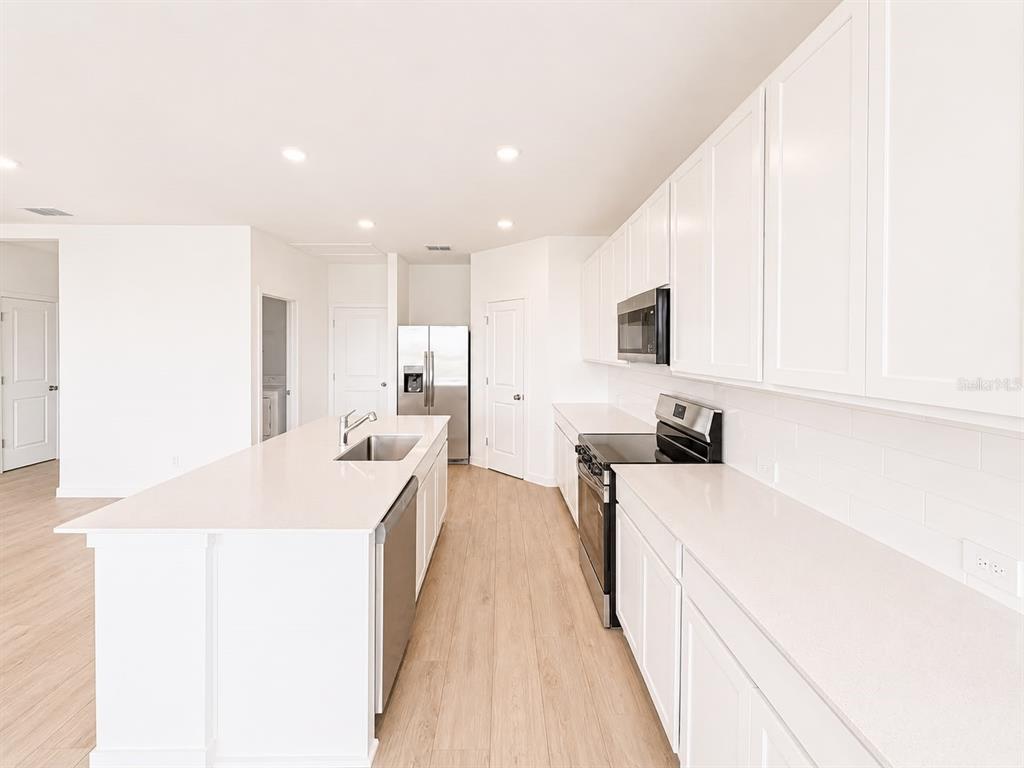 A modern kitchen features white cabinetry, quartz countertops, a center island, and light wood flooring — 644 RUTH AVENUE, HAINES CITY, FL