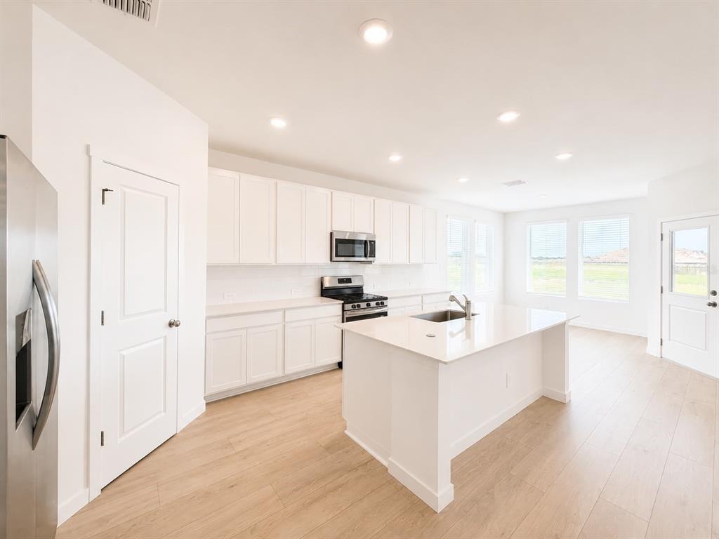 A bright kitchen features white cabinets, stainless steel appliances, a center island, and wood flooring — 644 RUTH AVENUE, HAINES CITY, FL