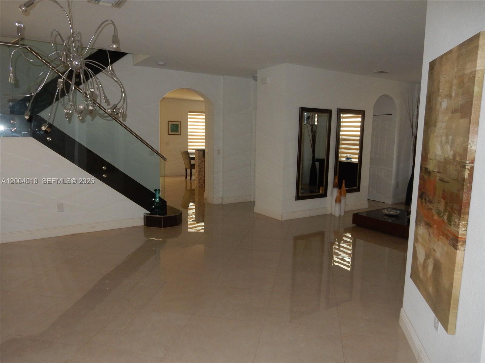 A modern foyer features a glass-railed staircase, polished tile floors, and arched doorways — 11455 NW 88th Ln, Doral FL 33178, DORAL, FL