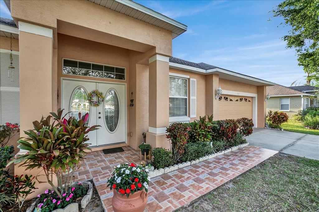 The exterior of a tan stucco house features a tiled walkway, double front doors, and landscaping — 4319 DINNER LAKE BOULEVARD, LAKE WALES, FL