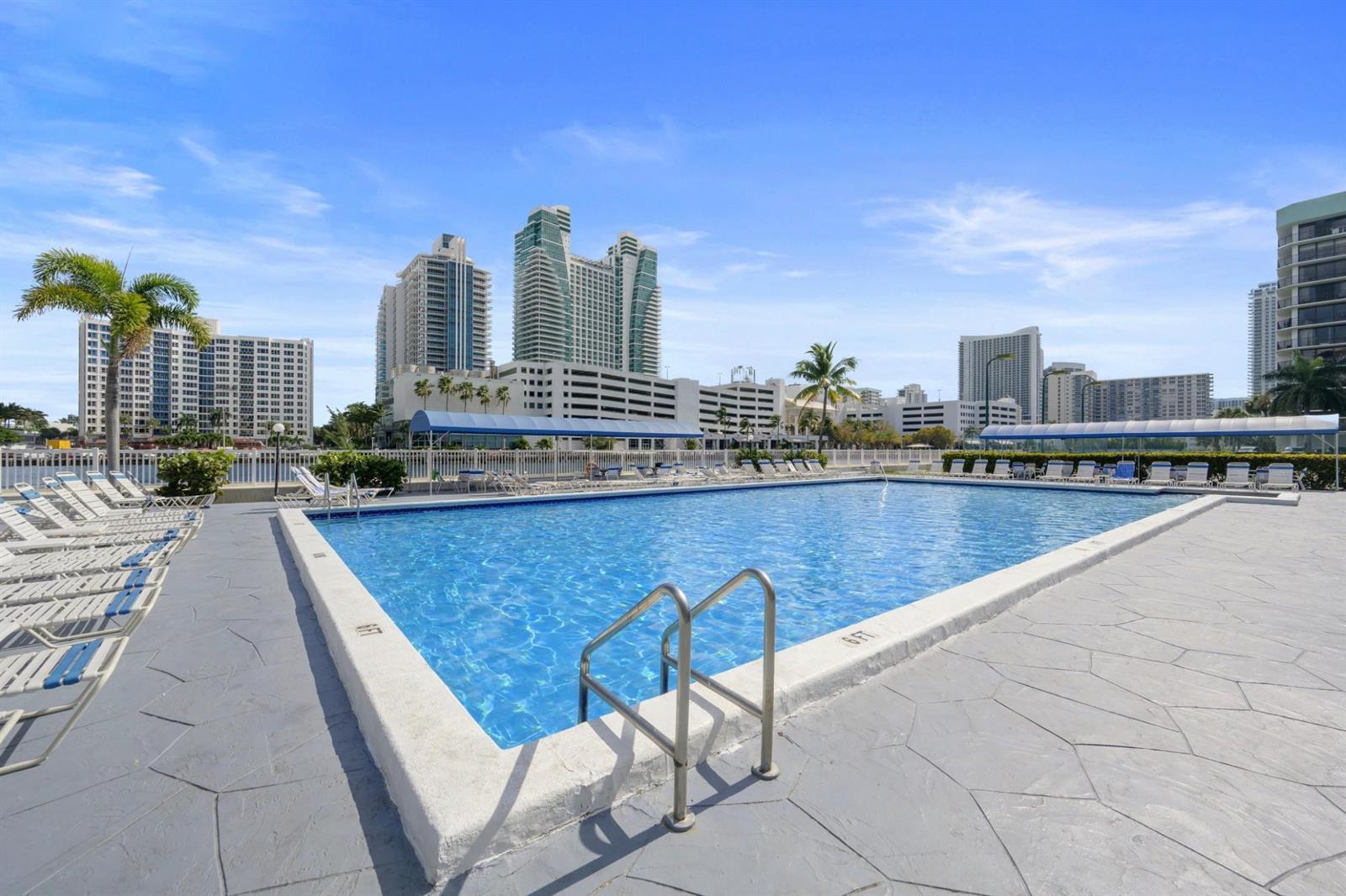 A rectangular swimming pool with a metal ladder sits on a concrete deck near buildings — 600 Parkview Drive, Hallandale Beach FL 33009, HALLANDALE BEACH, FL
