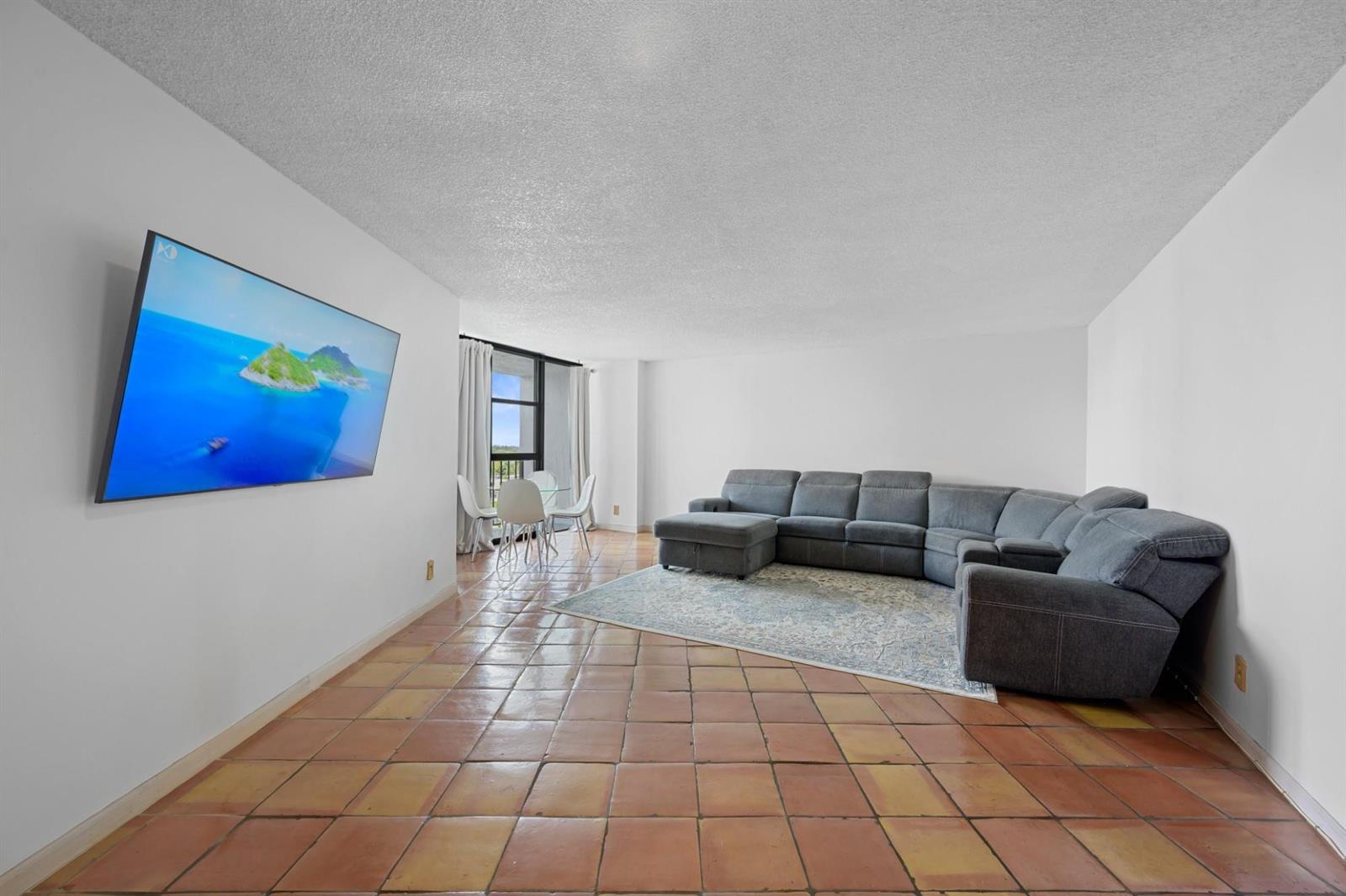 A living room with terracotta tile flooring, a grey sectional sofa, and a wall-mounted television — 600 Parkview Drive, Hallandale Beach FL 33009, HALLANDALE BEACH, FL